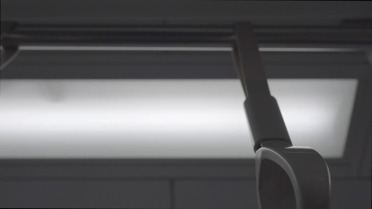 The hand ring  in the train carriage. The train is moving and the camera shakes slightly. The subject is on the right.  Look up. There are lights in the background.