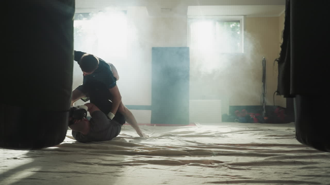 스포츠 클럽에서 바닥에 누워있는 파트너를 때리는 스포츠맨: 강한 남자가 흡연 체육관에서 스파링을 하는 친구를 때립니다.