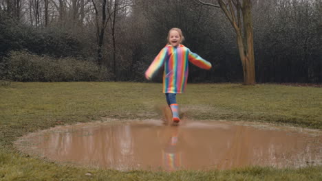 happy girl in colorful rain gear standing by a muddy puddle