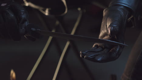 a person wearing black leather gloves holds a knife, tests its sharpness