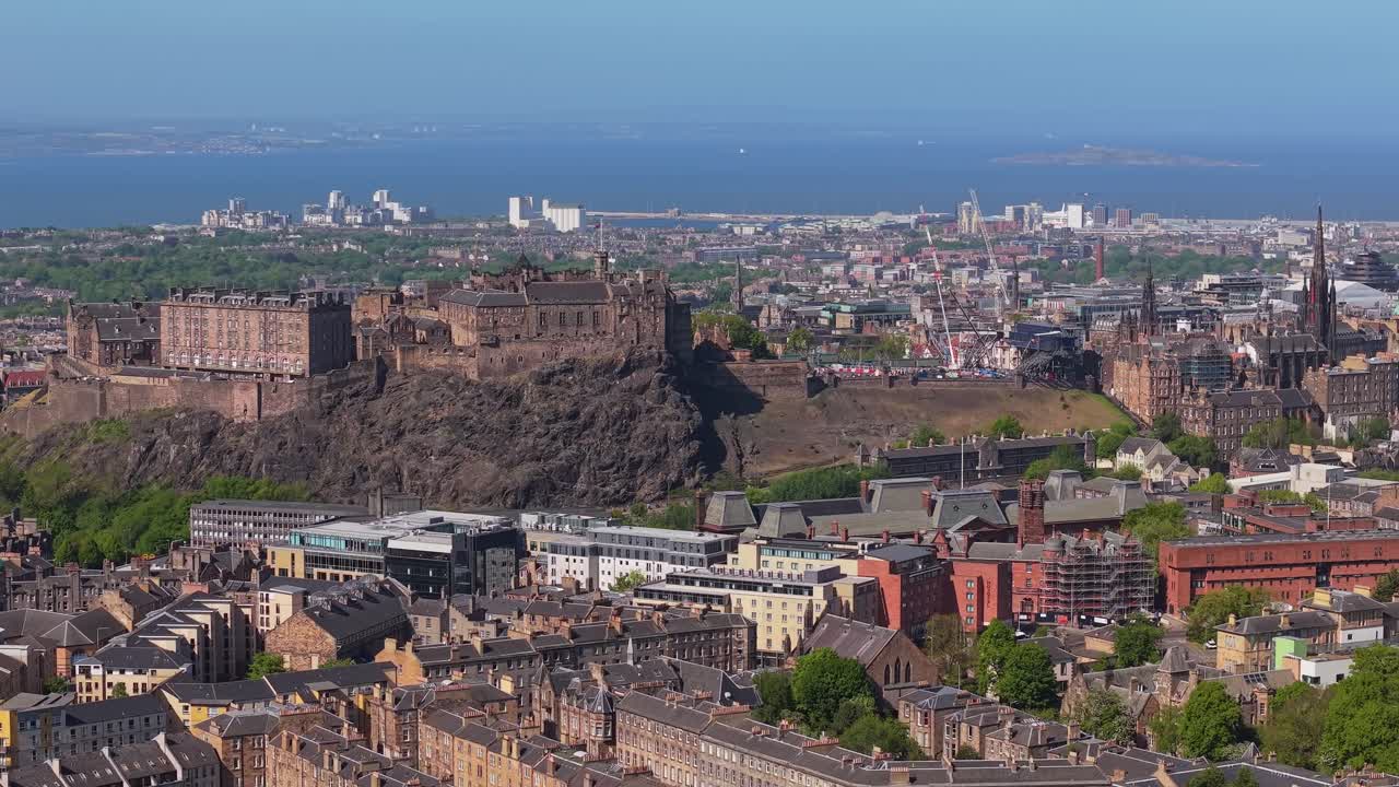 Drone orbits Edinburgh Castle, revealing the city’s majestic skyline, historic architecture, and surrounding landscape on a clear, sunny day