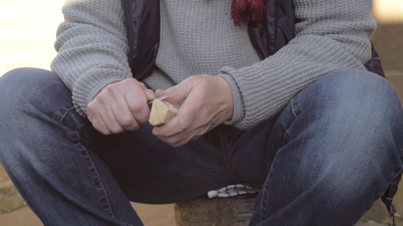 Woman sitting carving a piece of wood with a knife panning slow motion