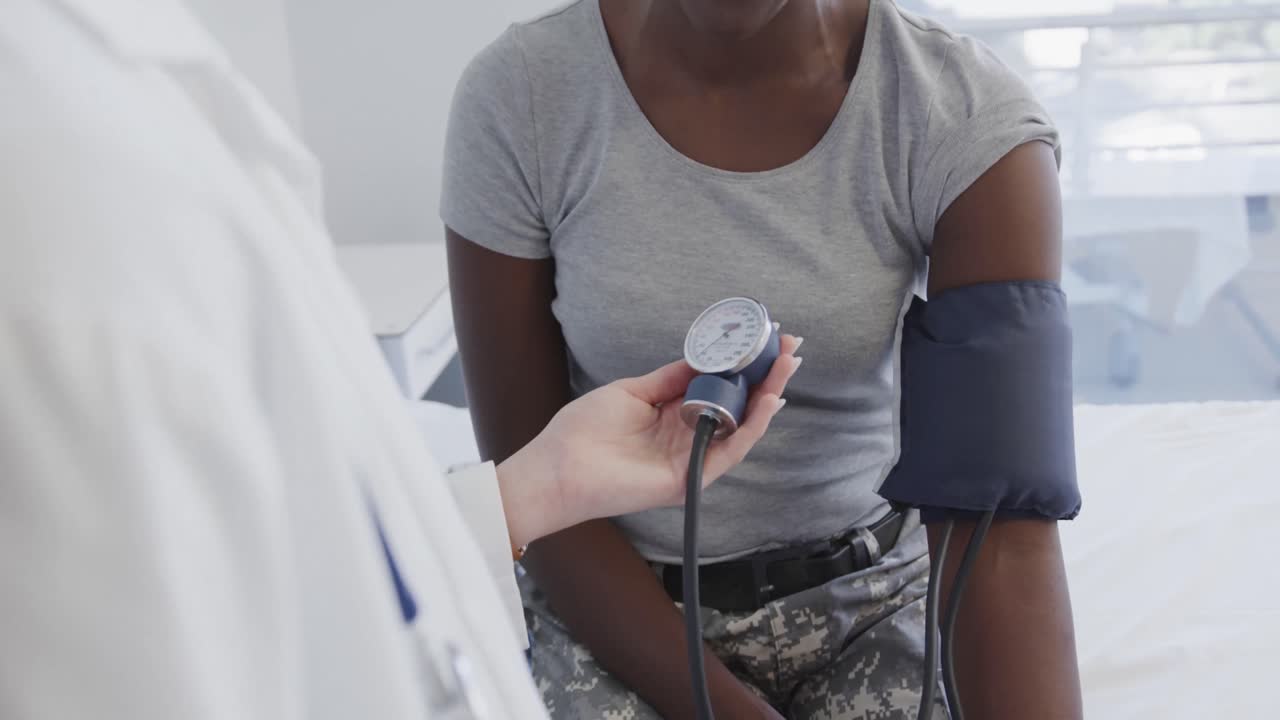 Happy diverse female soldier patient and doctor measuring blood pressure in hospital, in slow motion