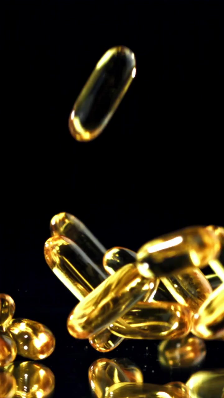 Capsule Omega-3 dorate che cadono al rallentatore su sfondo nero