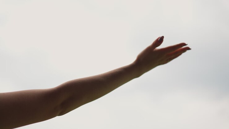 Hand van jonge vrouw onder warme regendruppels tegen een grijze lucht