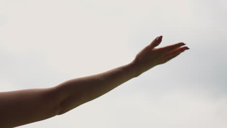 hand of young woman under warm rain drops against grey sky