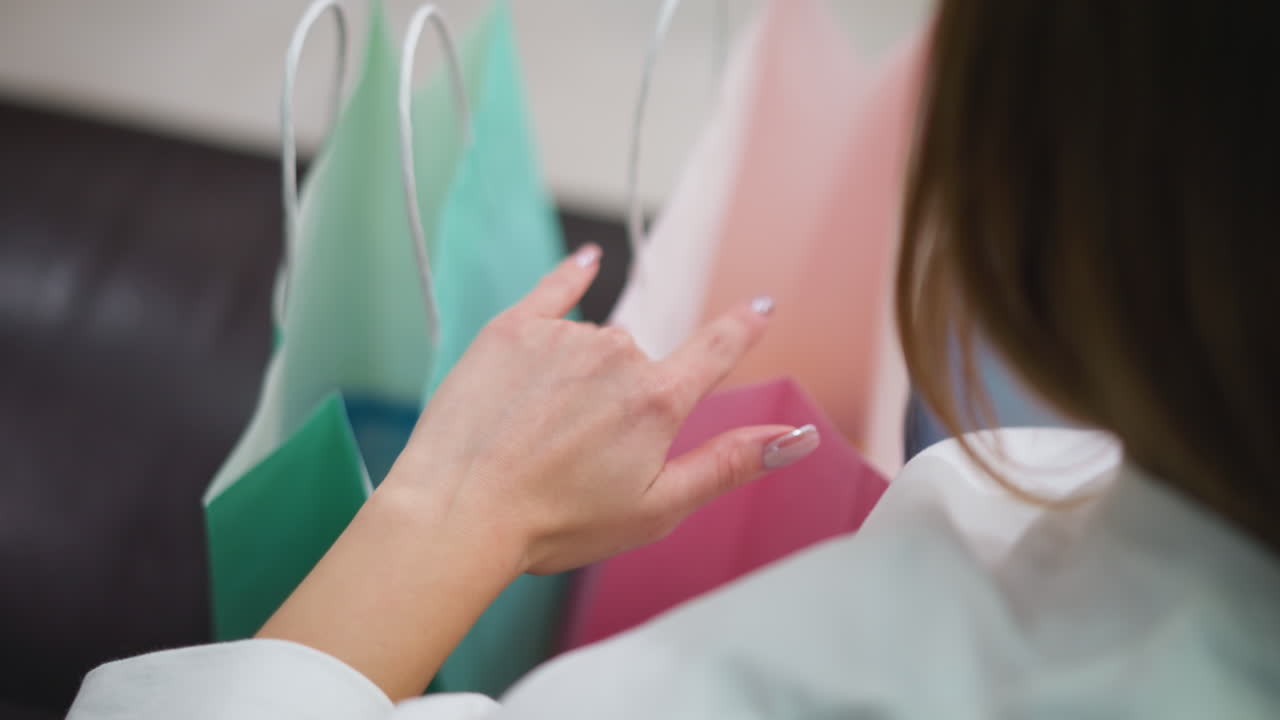 화려한 손을 가진 손이 다채로운 쇼핑 가방에 부드럽게 손을 고, 편안한 쇼핑 환경에서 가죽 좌석에 민트 녹색과 분홍색 가방을 전시합니다.