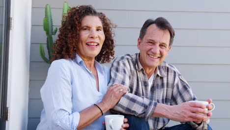 Retrato-De-Una-Pareja-De-Ancianos-Sonriente-Relajándose-Fuera-De-Casa-Con-Una-Bebida-Caliente