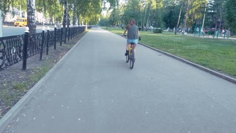 side view of a girl cycling on a road with flowers in a basket and exploring the city, slow mo, steadicam shot