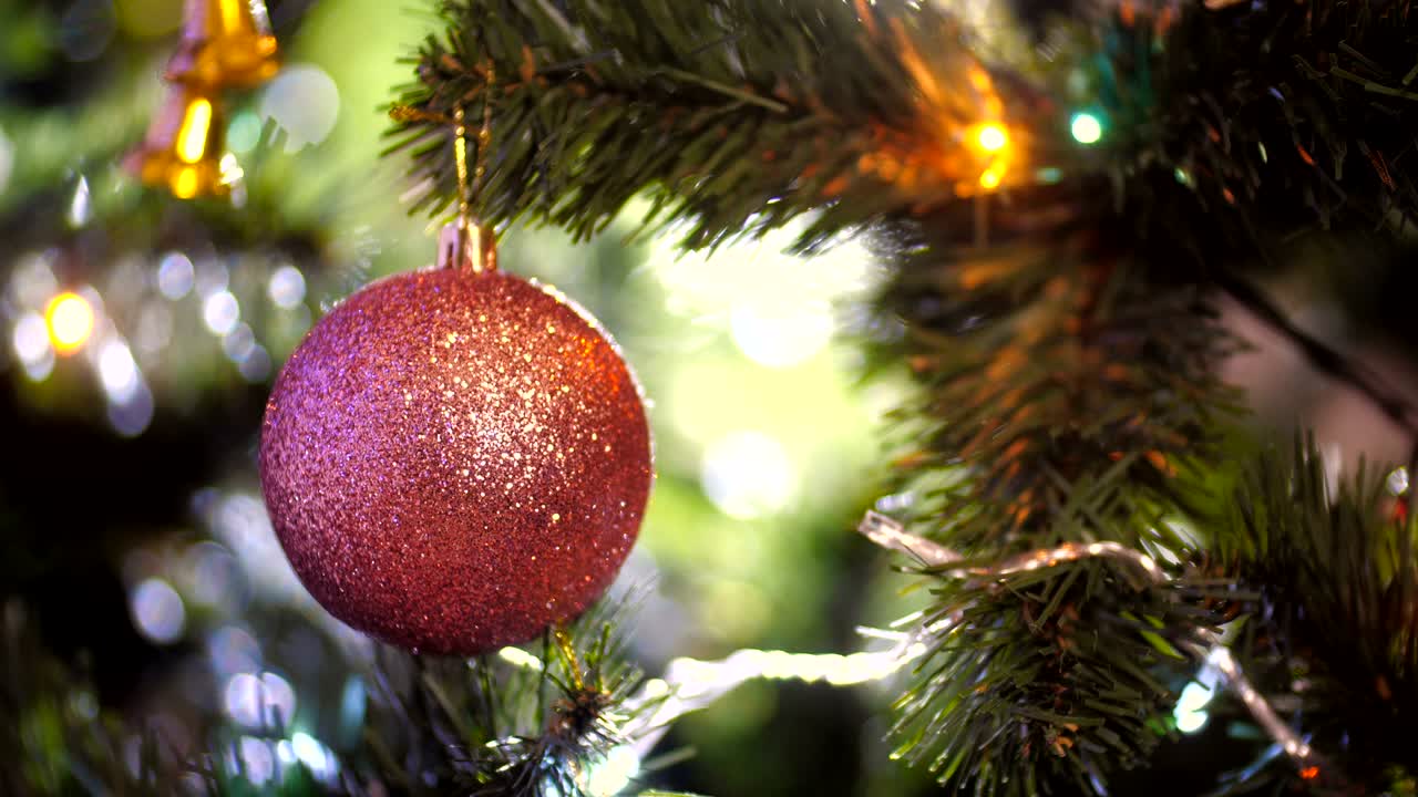 bola de navidad con chispas colgando de un árbol de navidad en un fondo claro de agujas verdes con guirnaldas parpadeantes y luego volviéndose borrosa. primer plano de la decoración rosada de navidad