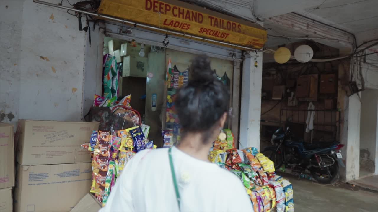 una mujer joven entrando en una tienda y buscando y comprando bocadillos en una tienda de calle que muestra una variedad de bocadillos fuera de la tienda
