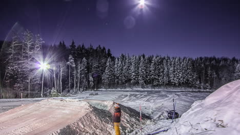 making a ski and snowboarding ramp jump at nighttime in the moonlight - sliding time lapse