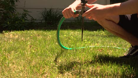 a man hooks up an old fashioned mechanical sprinkler in the heat of summer