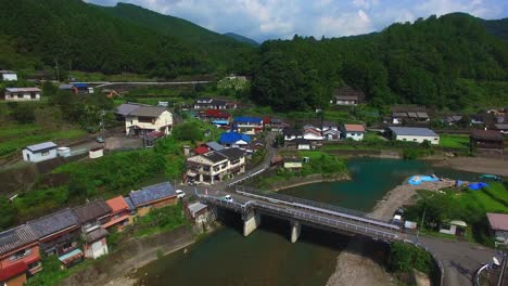 serene drone view travels forward above a peaceful japanese village with a river crossed by a bridge situated in a secluded valley