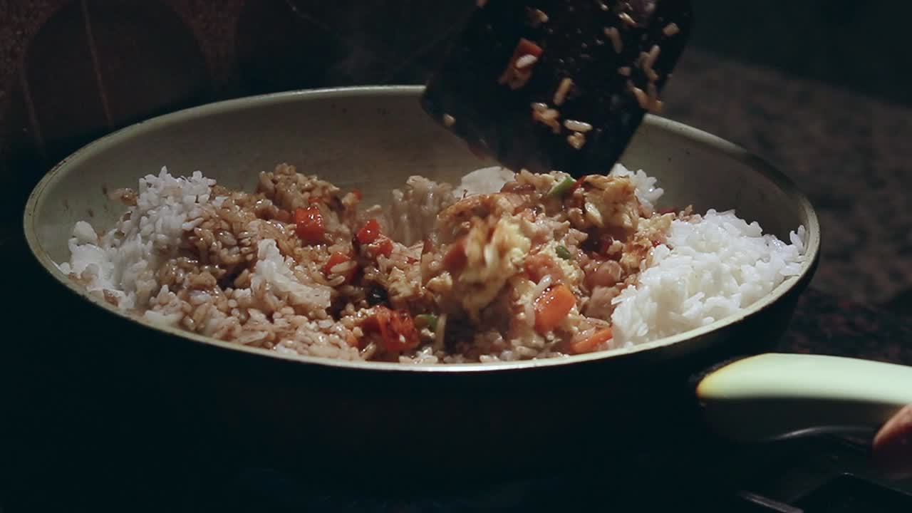 Close up to a pan containing rice drizzled with soy sauce and veggies and mixing it following a simple fried rice recipe