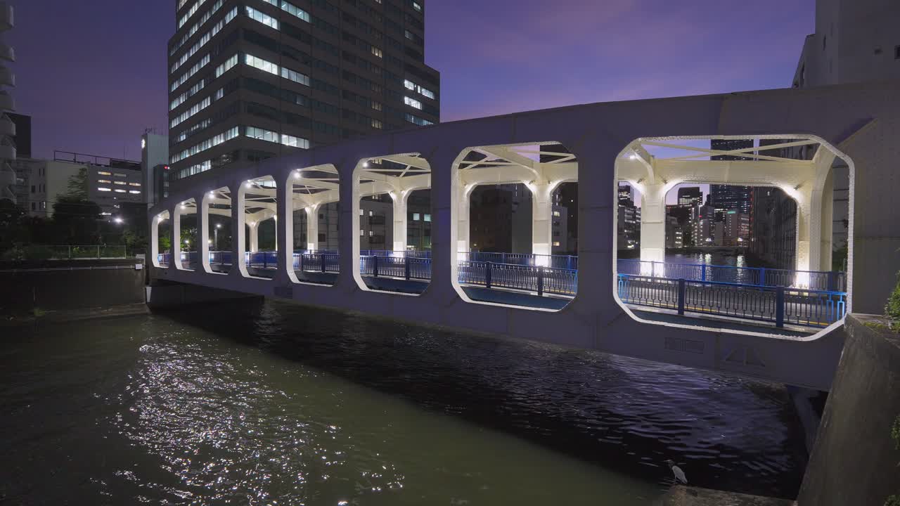 A shot of the illuminated Toyomi Bridge (Toyomibashi) in Tokyo at night, with the water below reflecting the lights