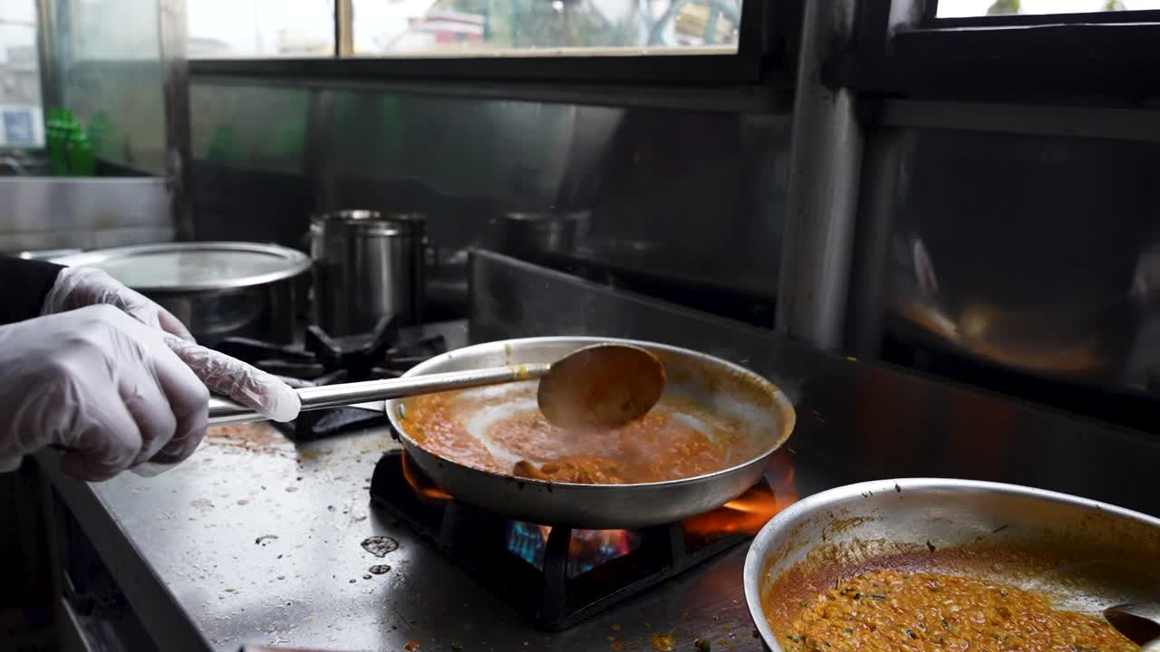 Chef stirs thick Mughlai-style daal mash in pan over flame at traditional restaurant. Lahore, Pakistan