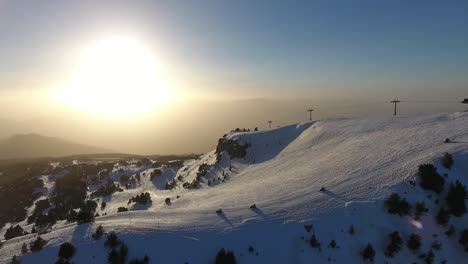 Snowmobiles-on-downhill-run-at-Chamrousse-ski-resort-in-the-French-Alps-during-sunset,-Aerial-follow-down-shot