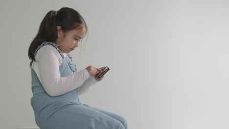 studio shot of young girl on asd spectrum gaming on mobile phone against white background 1