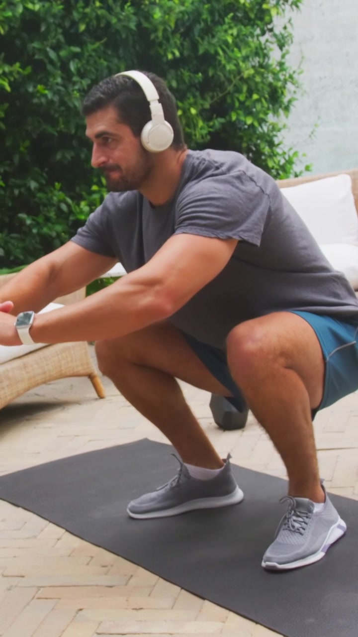 Vertikal video: Mand starter stående, sænker sig ned i squats på terrassemåtte i træningstøj til fitness