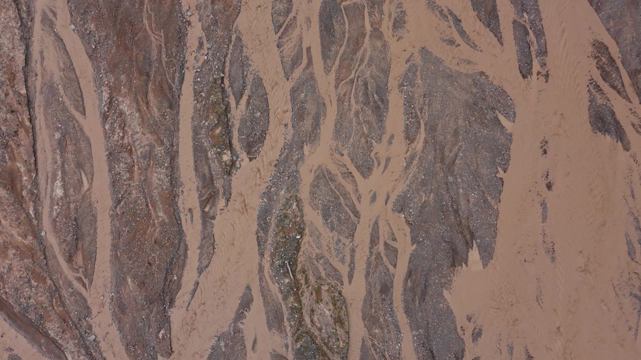 Braided river channels of Puente Chorro Blanco, dark muddy streaks and dry earthy soil, aerial top-down descend, drone backdrop