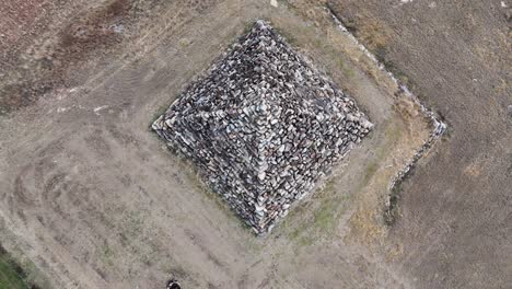 drone footage captures a slow, smooth aerial rotation above a large stone pyramid structure in a dry, open landscape under natural daylight
