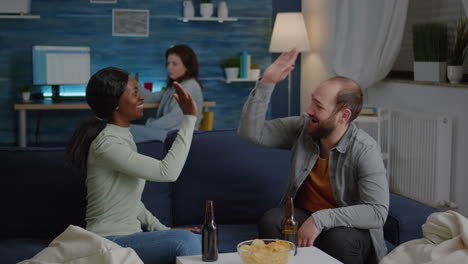 multi-ethnic friends relaxing on couch while giving high five laughing and having fun