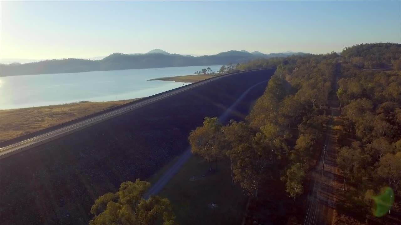 снимок с воздуха, снижающийся и летящий назад над стеной плотины и деревьями, на озере вивенхоу в квинсленде