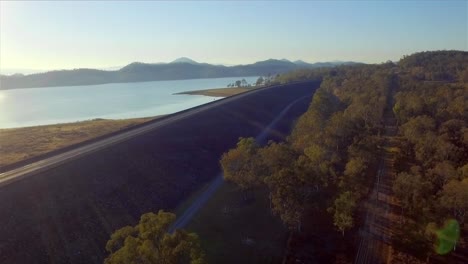 Aerial-shot,-descending-and-flying-backward-over-the-dam-wall-and-trees,-at-Lake-Wivenhoe-in-Queensland