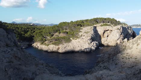 Fantastic-Drone-Footage-rising-up-behind-a-cliff-with-view-on-hidden-cove-in-the-spanish-Island-of-Mallorca