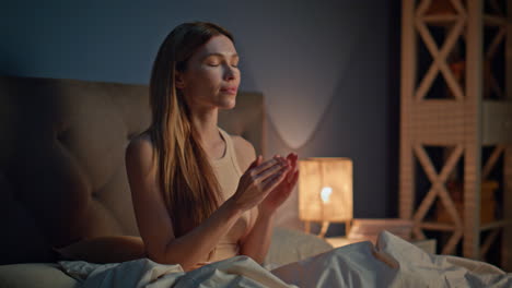 woman applying moisturizer cream on face preparing to sleep in cozy apartment