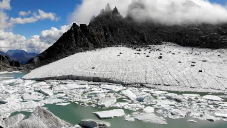 Aerial-flyover-above-a-glacier-lake-full-of-melted-icebergs-in-remote-parts-of-the-Swiss-Alps-with-a-pan-down-from-the-peak-down-to-the-ice-chunks