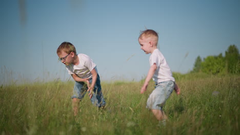 a young boy in a white shirt and short jeans is captured mid-backflip in a sunny, grassy field, while his younger brother, also in a white shirt and shorts, joyfully jumps beside him