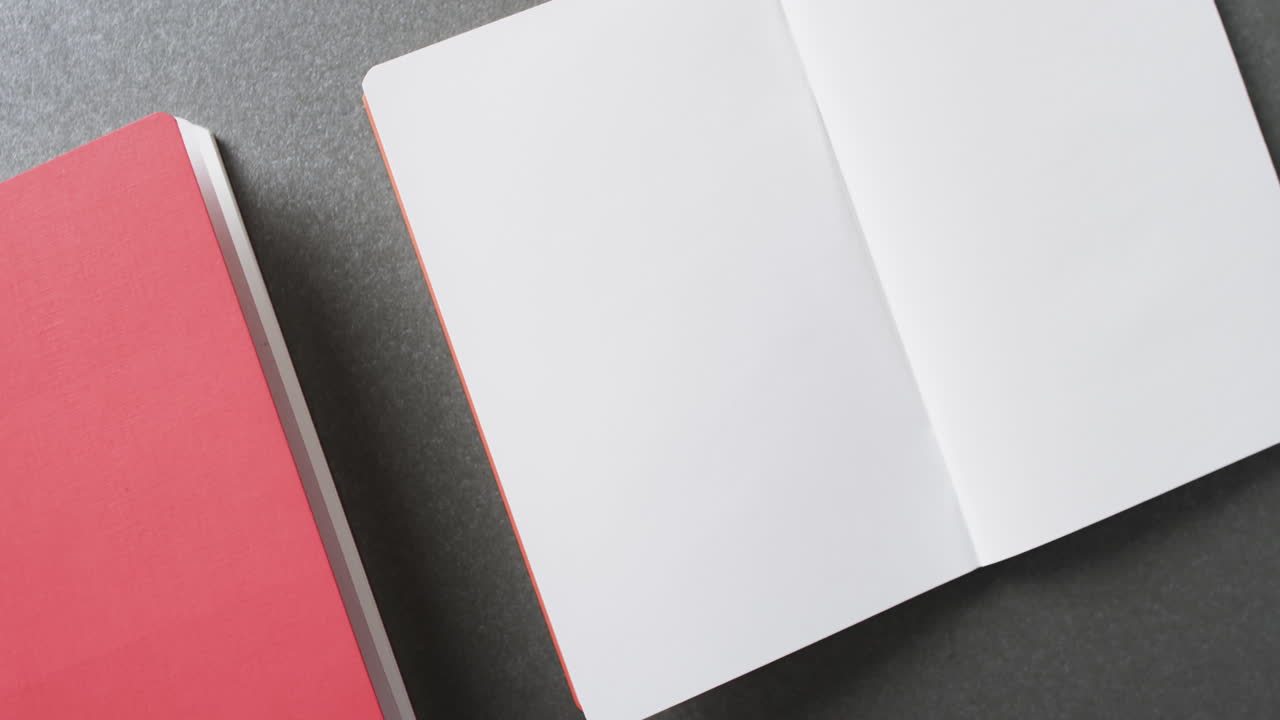 Close up of open blank book and pink book with copy space on gray background in slow motion