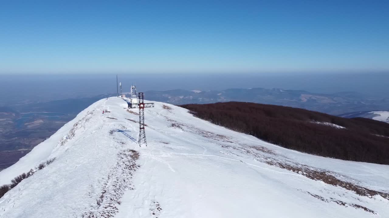 Mountains cross standing on snow covered peak in mountains hiking trail, aerial view of stunning winter unpolluted landscape of Italian alps