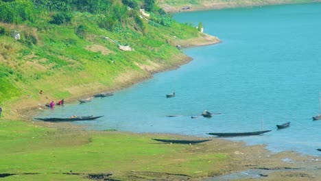 shot of riverbank with canoe boats on river and woman washing clothes in india, bangladesh