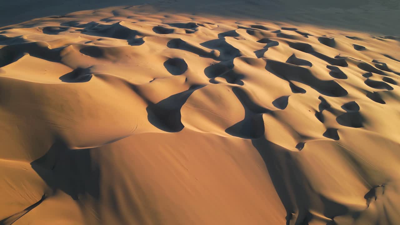 Cinematic drone perspective of shifting sand formations glowing under a dramatic sunset horizon
