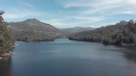 Mattupetty-in-Munnar,-surrounded-by-lush-mountains-and-hills-in-India---Aerial-Low-angle-Fly-over-shot