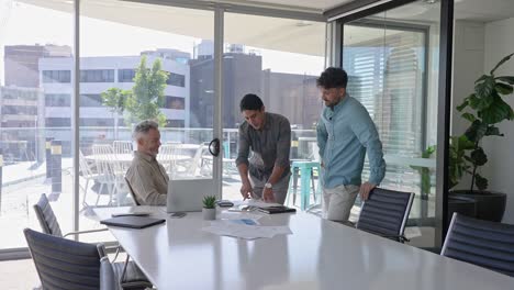 three businessmen standing in the boardroom looking at a laptop computer.