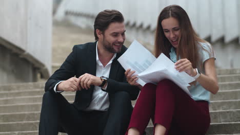 business people reading papers outdoors. man and woman laughing on street