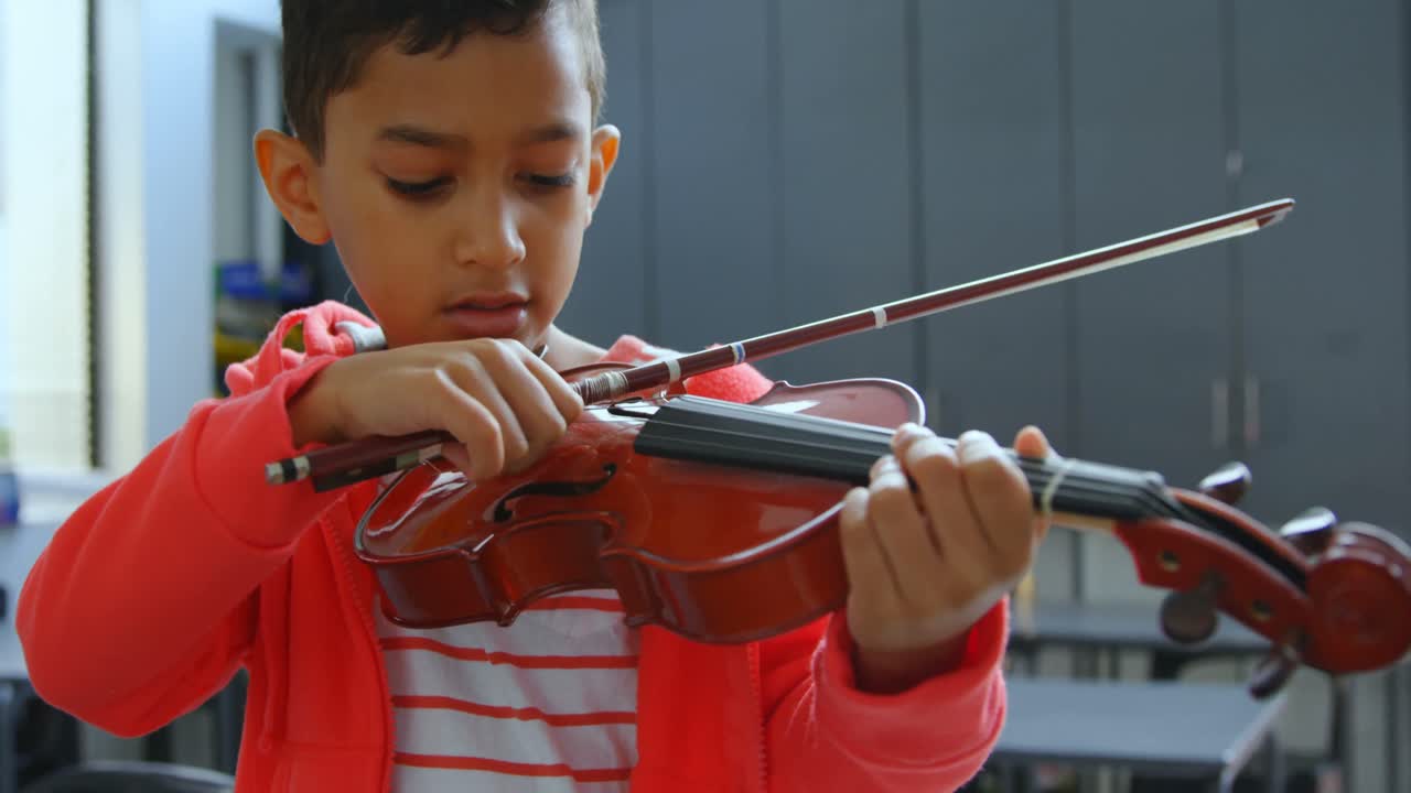 vista frontal de un escolar asiático atento tocando el violín en el aula de la escuela 4k