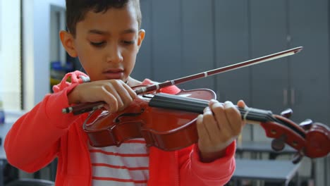 Front-view-of-attentive-Asian-schoolboy-playing-violin-in-classroom-at-school-4k