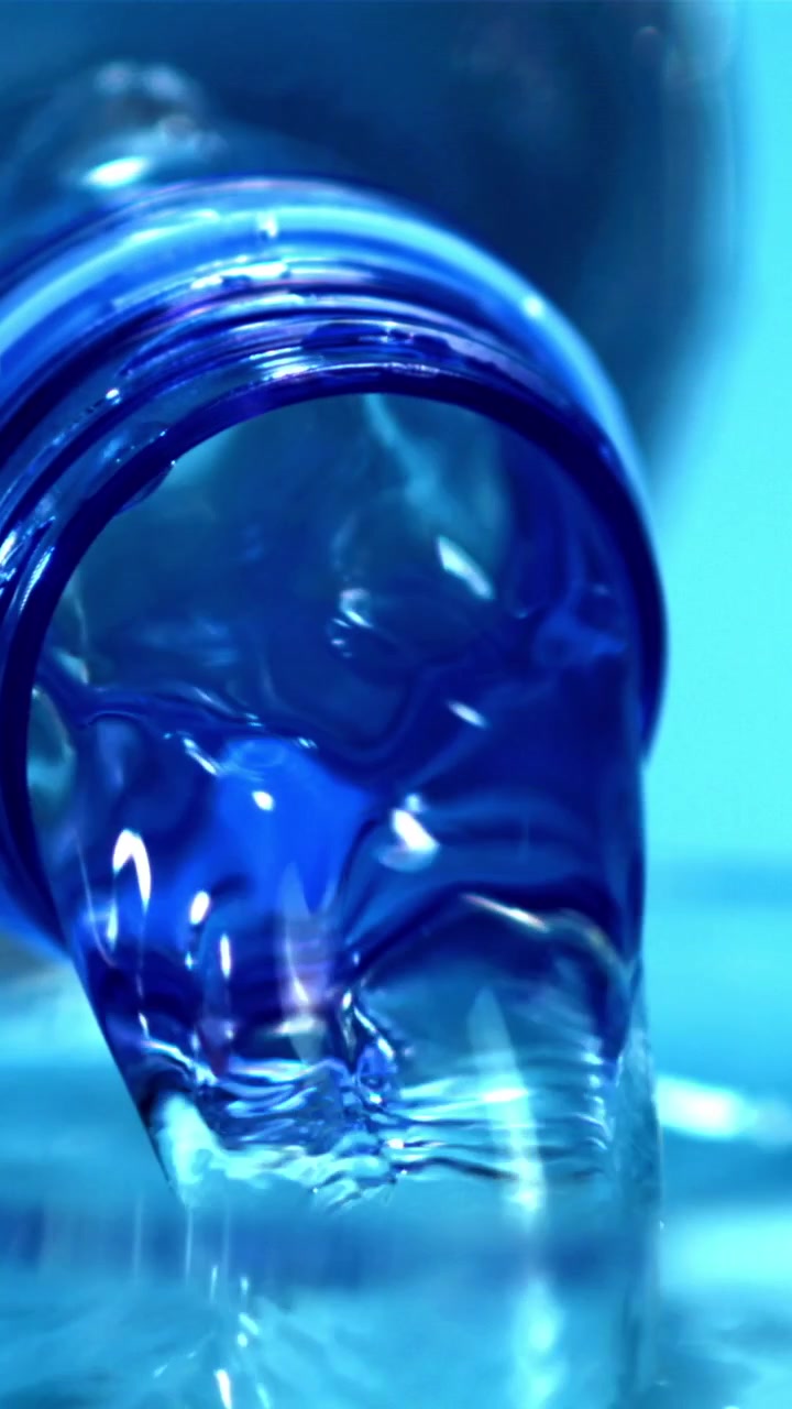 Acqua limpida che si versa da una bottiglia di plastica blu