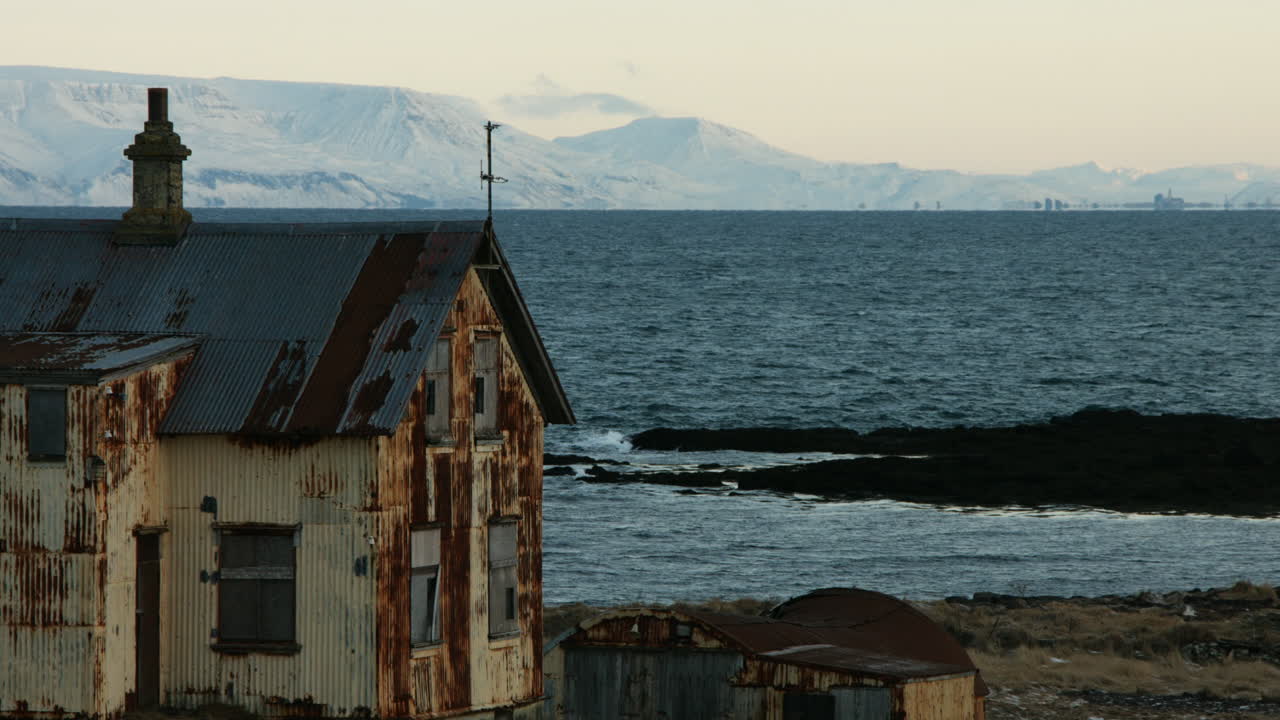 침체된 집의 꾸준한 겨울 촬영은 눈 인 산, 황혼에 평온한 바다를 특징으로합니다. - 4k