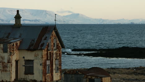 tomada de invierno constante de una casa degradada con montañas nevadas, océano tranquilo al anochecer - 4k