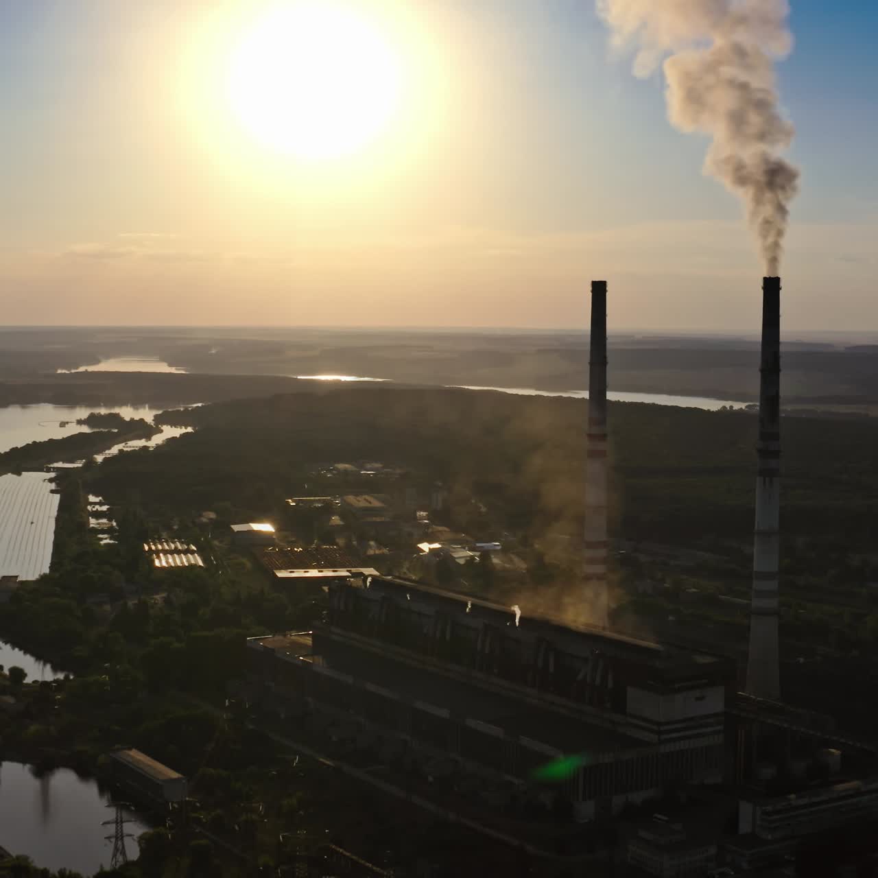 Dark silhouette of a factory at sunset. Manufacture releases harmful smoke into the air. Nature in danger. Industrial plant near the river in the evening.