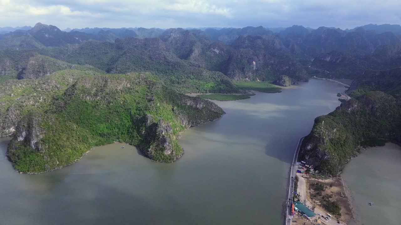 Smooth zoom in aerial showing river mouth, coastal hills and mountain shadows under blue sky