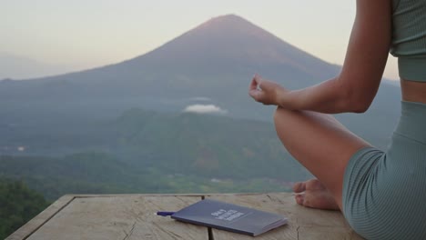 cuaderno al lado mujer en postura de yoga meditando frente al volcán, concepto de diario