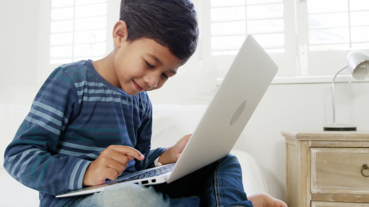 niño usando la computadora portátil mientras se relaja en la cama