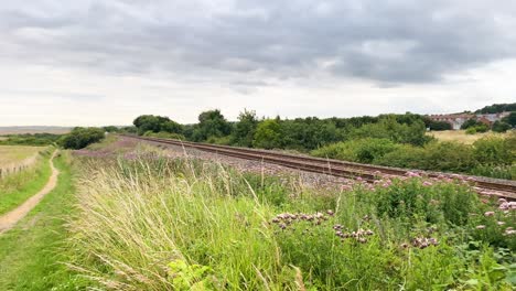 A-railway-track-going-through-the-countryside,-next-to-footpath-along-the-North-East-Coastline,-England-on-a-cloudy-evening